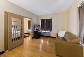 A living room with a wooden floor, a brown sofa, a television, and a door leading to another room. - Red Roof Inn PLUS+ Columbus Downtown-Convention Center (Columbus)