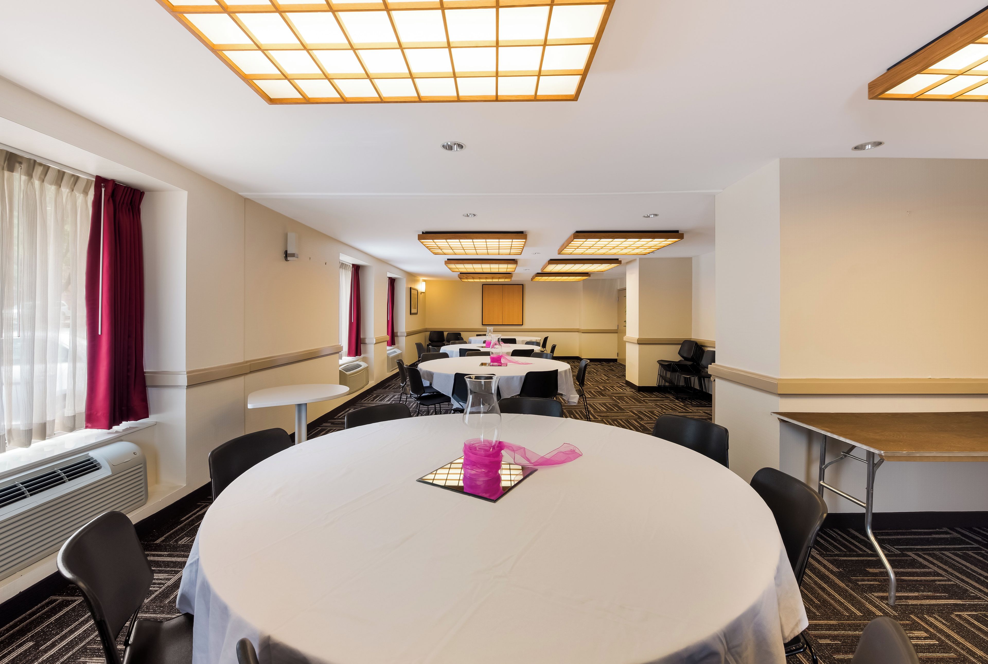 A hotel conference room with round tables, chairs, and a long table with a pink decorative item.