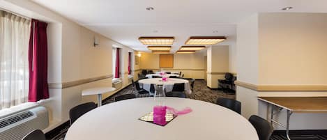 Une salle de conférence d’hôtel avec des tables rondes, des chaises et une longue table agrémentée d’un objet décoratif rose.