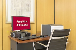 A hotel room with a desk, a computer, a printer, and a chair. A sign on the desk advertises free Wi-Fi in all rooms. - Red Roof Inn PLUS+ Columbus Downtown-Convention Center (Columbus)