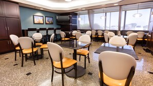 Un salón de conferencias con varias mesas y sillas, un televisor de pantalla plana y ventanas grandes con cortinas.