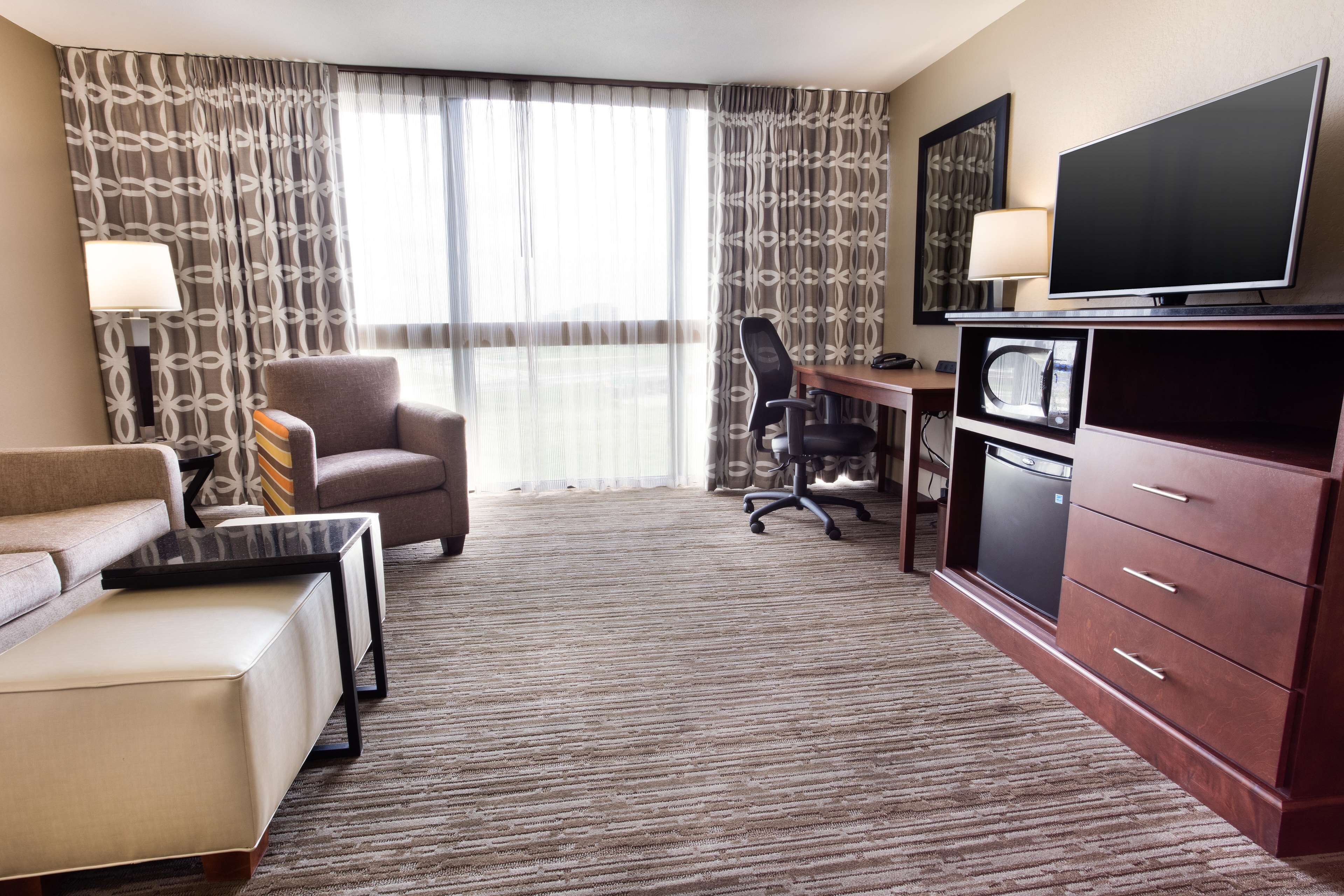 A hotel room with a sofa, a desk, a chair, a television, a microwave, and a cabinet.