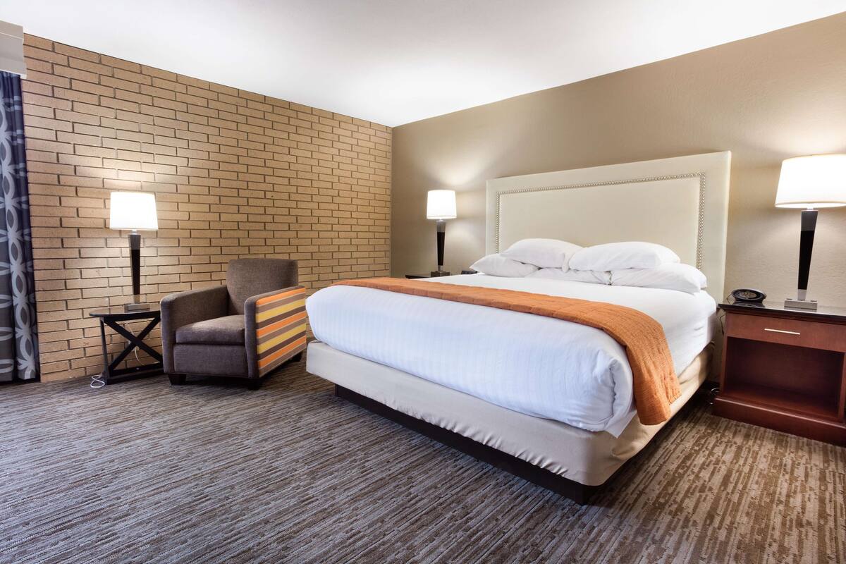 A hotel room with a large bed, two bedside lamps, a chair, and a small table.