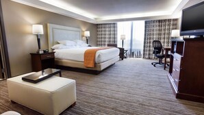 Habitación de hotel con una cama grande, un escritorio, una silla, un televisor y una ventana con cortinas.