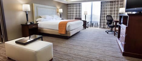 A hotel room with a large bed, a desk, a chair, a television, and a window with curtains.