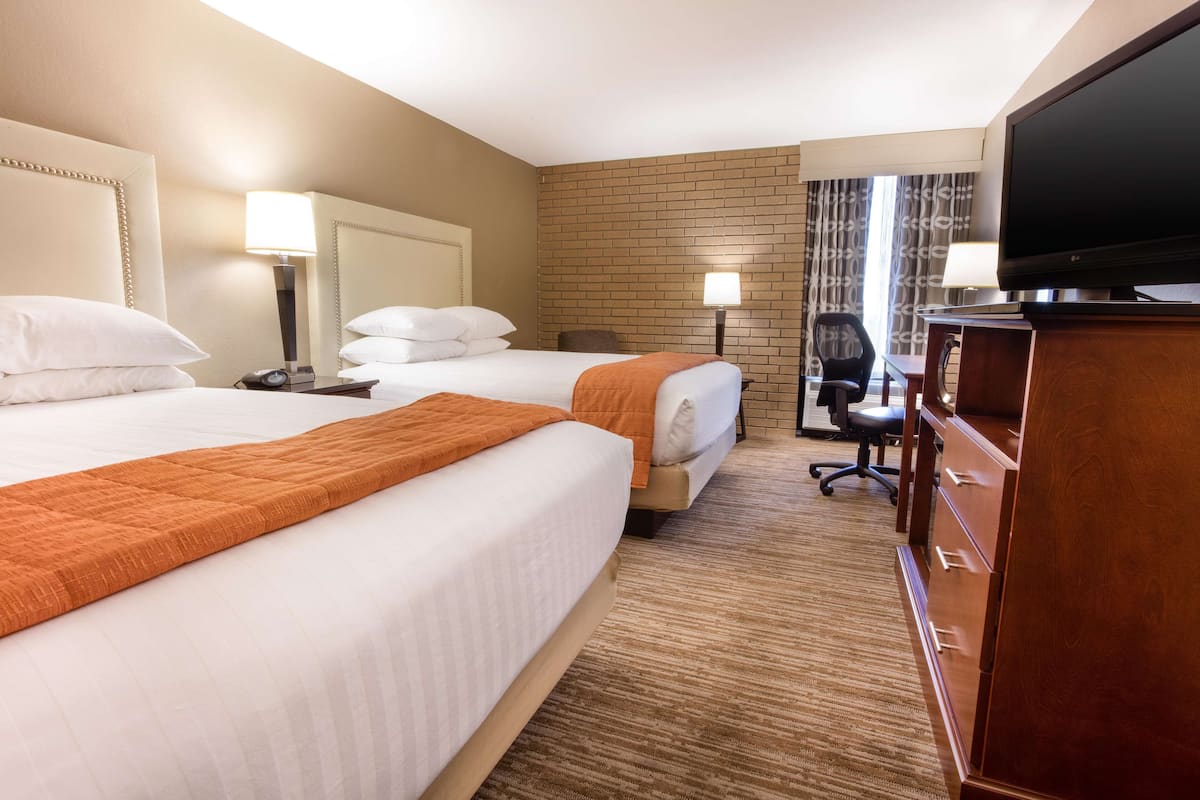 A hotel room with two beds, a TV, a desk, and a chair.