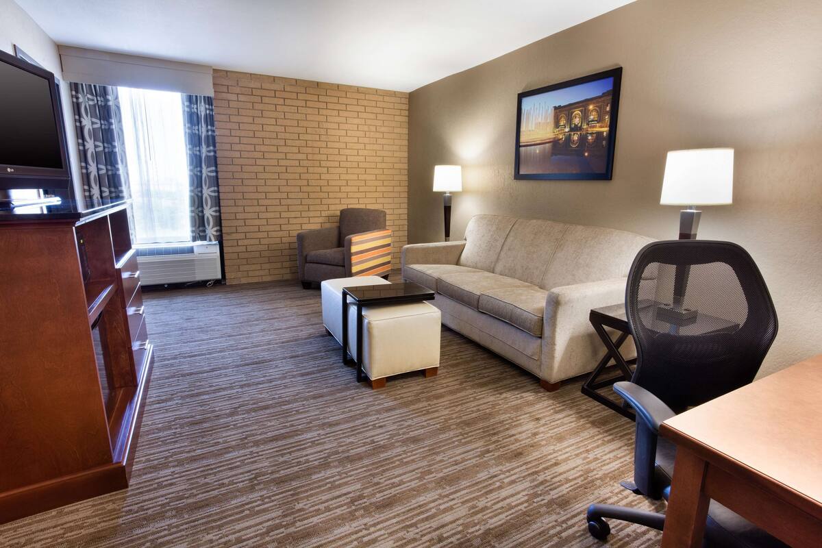 A hotel room with a flat-screen TV, a sofa, a desk, a chair, and a lamp.