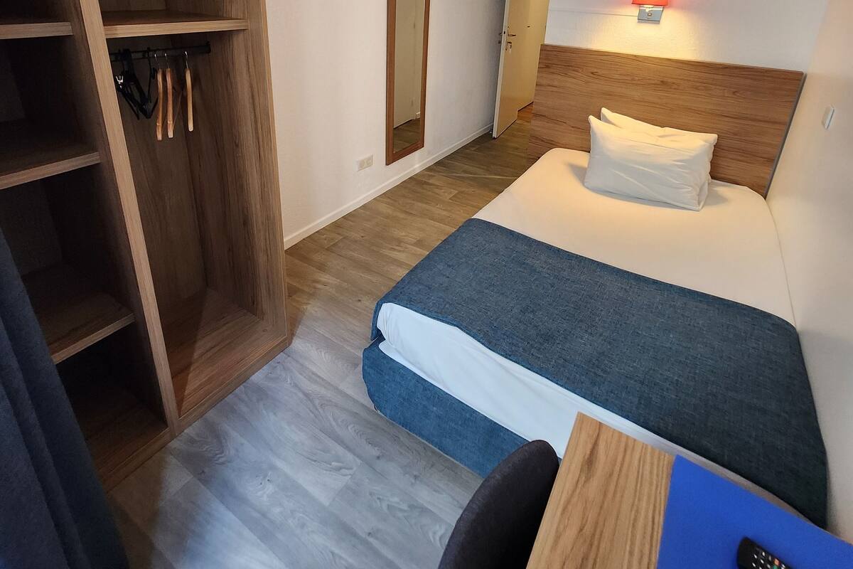 A hotel room with a bed, a desk, a chair, a wardrobe, and a mirror.