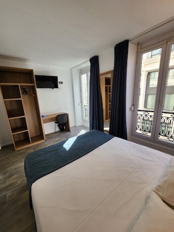 A hotel room with a bed, a desk, a wardrobe, and a balcony with a view.