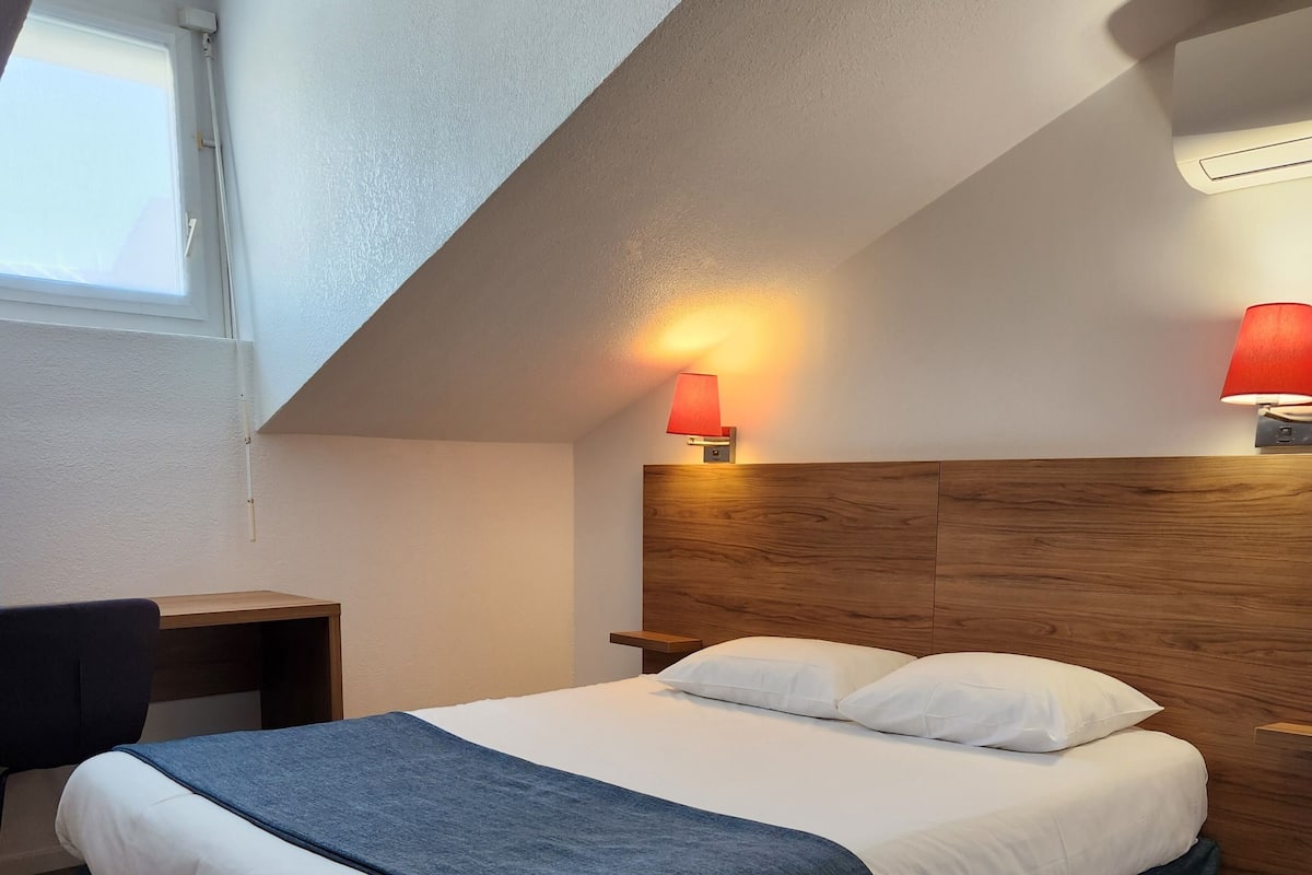 A bedroom with a bed, a desk, and a nightstand.