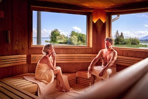 Una sauna con bancos de madera y amplios ventanales con vistas a un lago y árboles.
