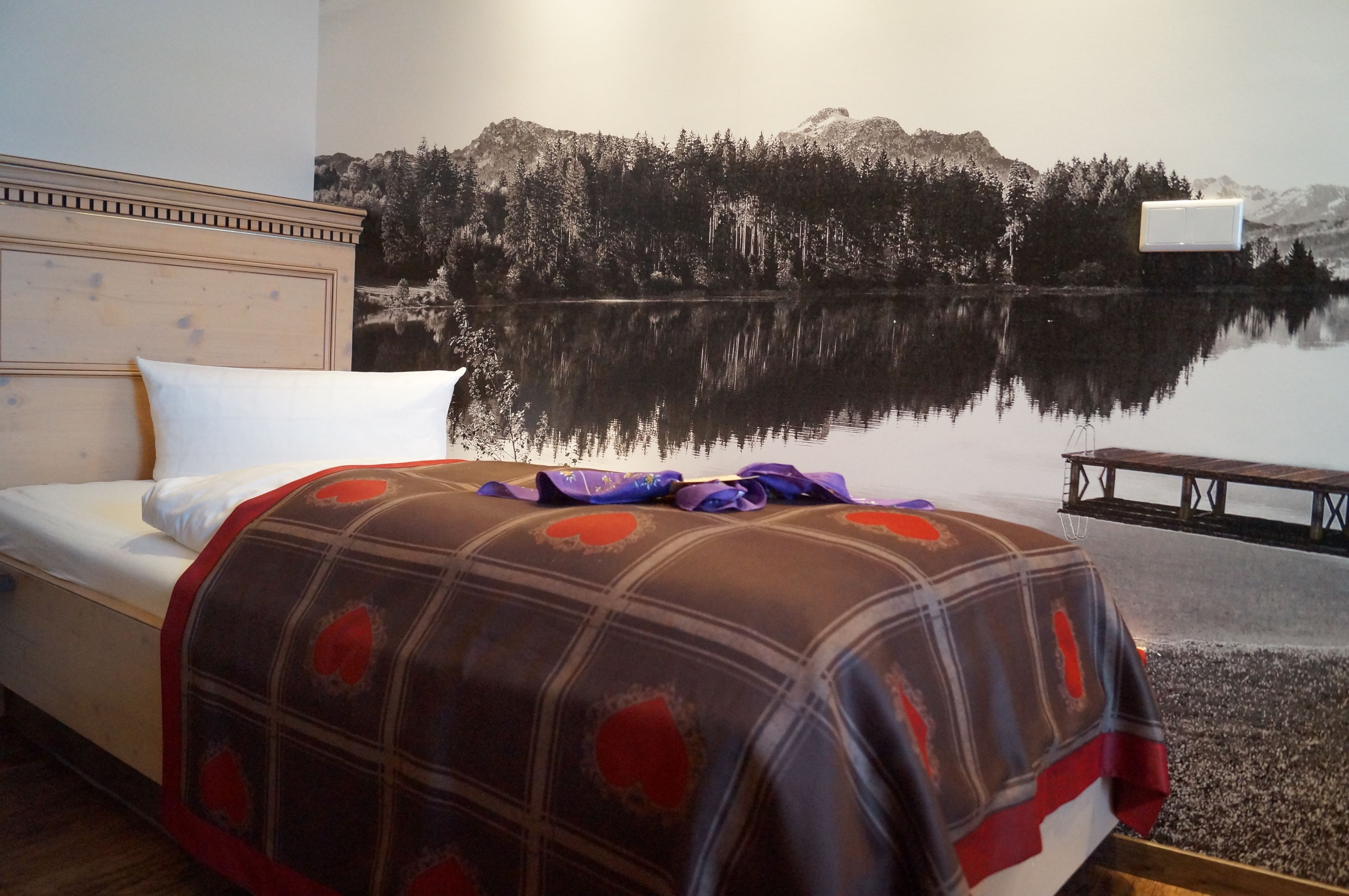 Un dormitorio con cama, cabecera, aire acondicionado de pared y un mural de un lago con árboles y montañas.