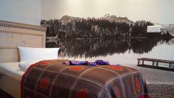 Un dormitorio con cama, cabecera, aire acondicionado de pared y un mural de un lago con árboles y montañas.