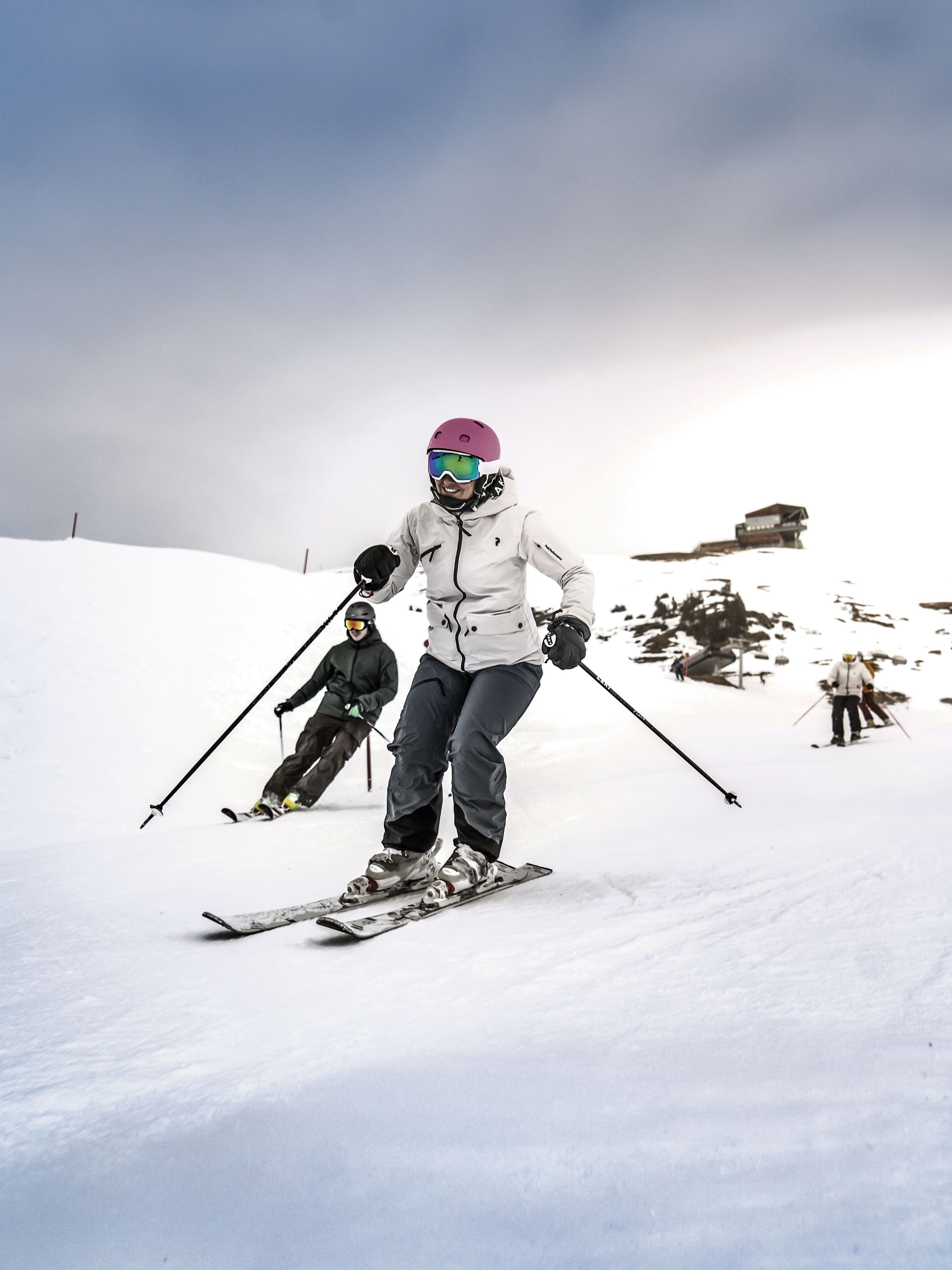 En person står på ski i et sneklædt terræn med en bygning i baggrunden.