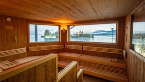A wooden sauna with benches and large windows overlooking a lake. - Hotel Sommer Füssen (Fuessen)