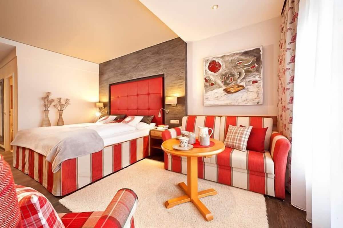 A hotel room with a bed, a sofa, a small table, and a painting on the wall.