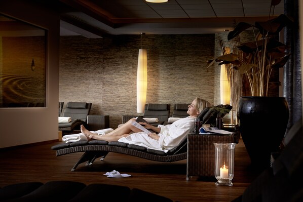 Un cuarto de spa con una silla reclinable, una camilla de masaje y un jarrón grande con plantas secas.