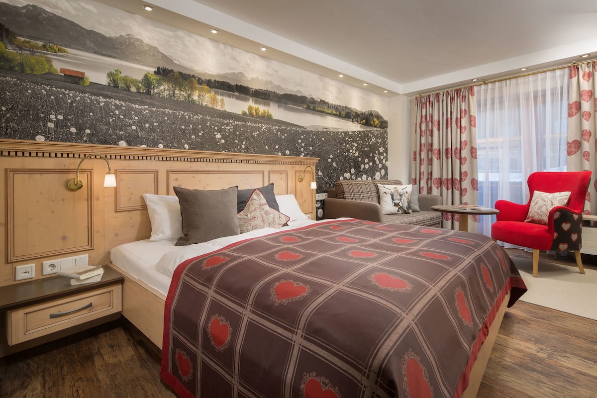 A hotel room with a large bed, a red armchair, a small table, and a mural on the wall.