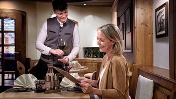 L’intérieur d’un restaurant, avec des meubles en bois, un serveur qui sert du vin et un menu.
