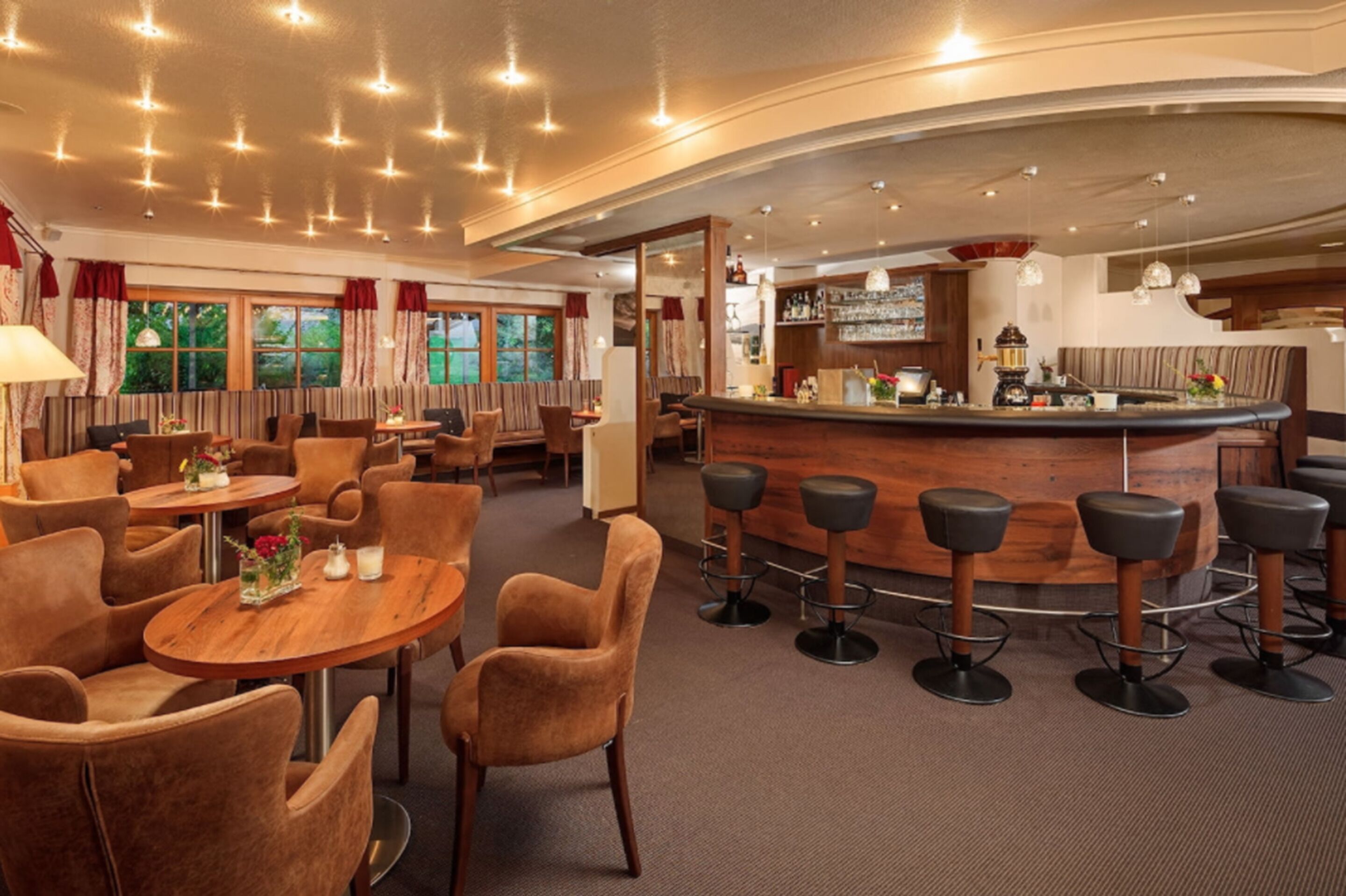 Uma área de bar com mesas redondas e banquetas, um balcão com um barista e um espaço de estar com cadeiras acolchoadas.