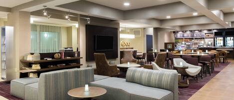 Un hall d’hôtel moderne doté d’espaces de détente, d’un bar et d’un téléviseur.