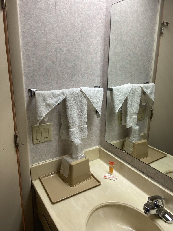 A bathroom with a beige sink, a mirror, and two white towels hanging on towel hooks.