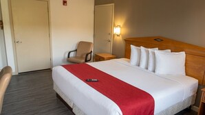 A hotel room with a bed, a chair, a bedside table, and a wall-mounted light. - Budget Inn Timmonsville (Timmonsville)