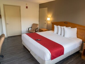 A hotel room with a bed, a chair, a bedside table, and a wall-mounted light. - Budget Inn Timmonsville (Timmonsville)