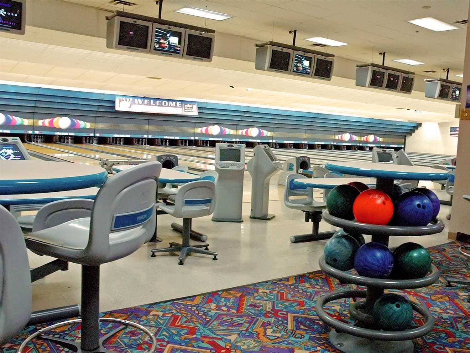 A bowling alley with multiple lanes, bowling balls, and seating areas.