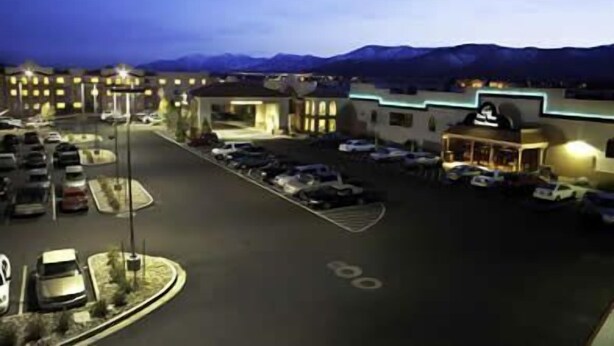 A hotel with a parking lot, a building with a flat roof, and mountains in the background. - Gold Dust West Carson City (Carson City)