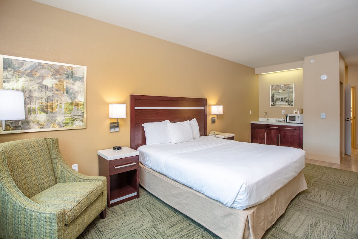 A hotel room with a bed, a chair, a nightstand, a desk, a mirror, and a painting on the wall.