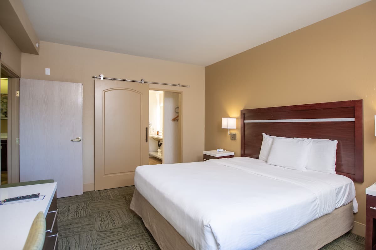 A hotel room with a bed, bedside table, nightstand, and a desk with a chair.