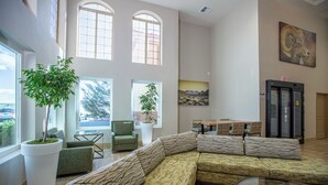A spacious lobby with a large sectional sofa, two potted plants, a dining area with wicker chairs, and a painting on the wall. - Gold Dust West Carson City (Carson City)