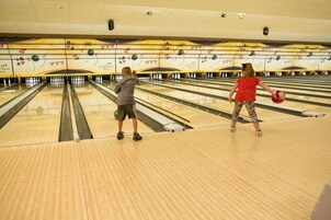 Bolera con múltiples pistas, suelo de madera y una bola de bolos en movimiento.