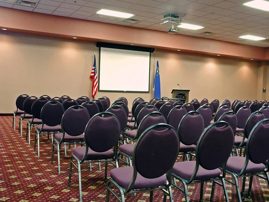 A conference room with rows of purple chairs, a projector screen, an American flag, and a podium with a plaque.
