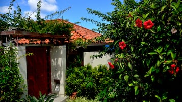 A small, enclosed outdoor area with a red door, surrounded by lush greenery and red flowers.