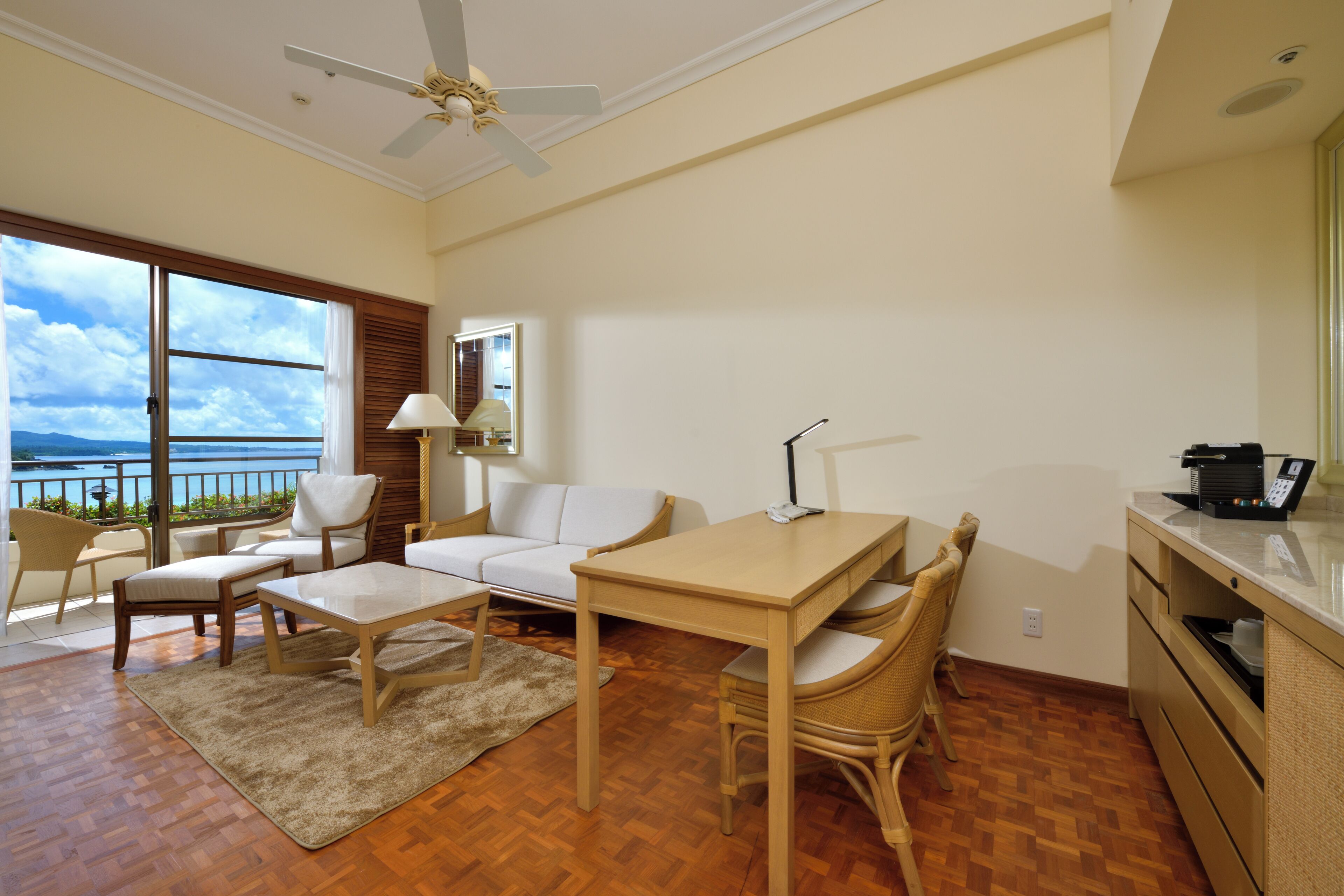 A spacious living area with a wooden floor, a white sofa, a dining table, and a kitchen area.