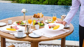 A breakfast table by a pool with plates of food, drinks, and a pitcher.