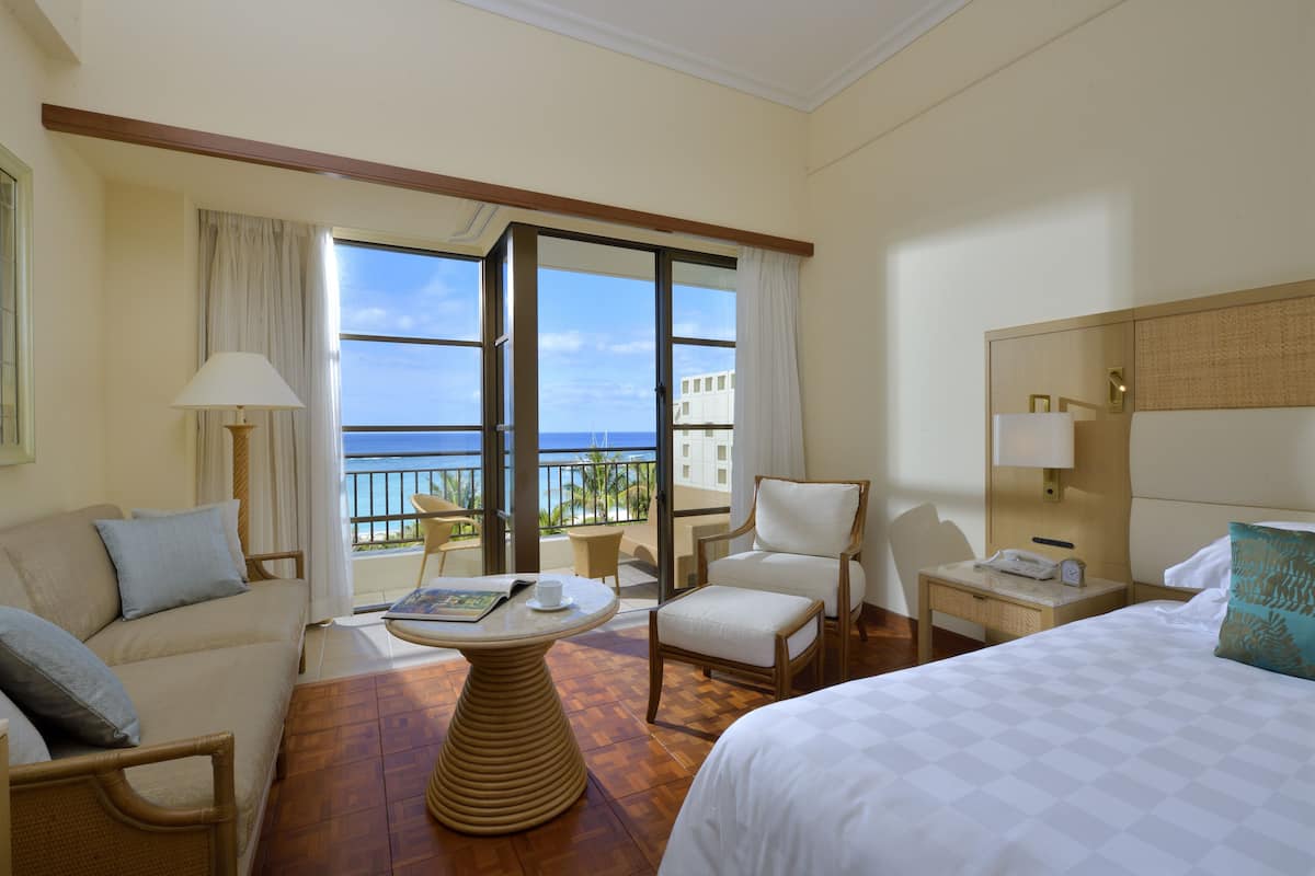 Ein Hotelzimmer mit Balkon, einer Couch, einem Sessel, einem Nachttisch und einem Bett.