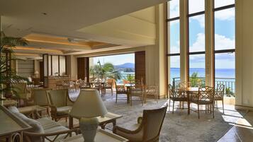 A spacious indoor area with multiple seating arrangements, large windows offering a view of the ocean, and a ceiling with recessed lighting.