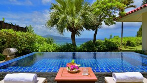Una piscina con vistas despejadas al mar, rodeada de exuberante vegetación y una mesa de madera con un arreglo floral.