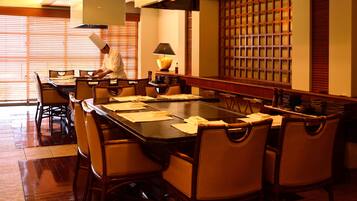 A conference room with a long table, chairs, and a chef preparing food.