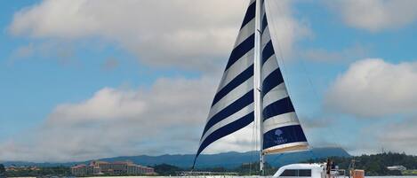 A sailboat named 'The Busena Terrace' on calm waters with a clear sky and distant mountains.