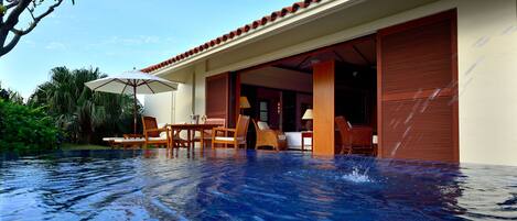 A poolside area with a wooden table and chairs, a lounge chair, and a covered umbrella.