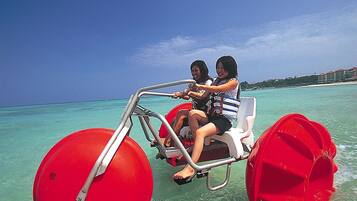 Two people on a red watercraft with a clear view of the ocean and a distant shoreline.