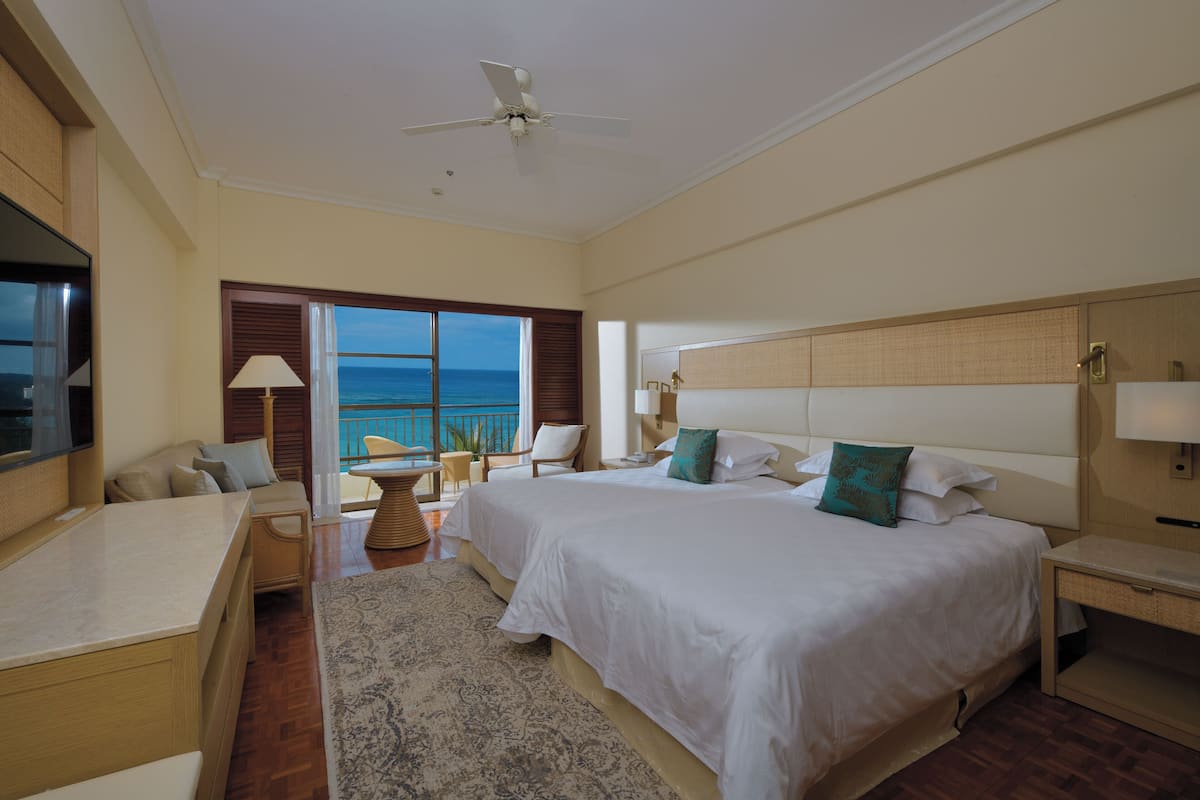 Ein Hotelzimmer mit einem großen Bett, einem Schreibtisch und Blick aufs Meer.