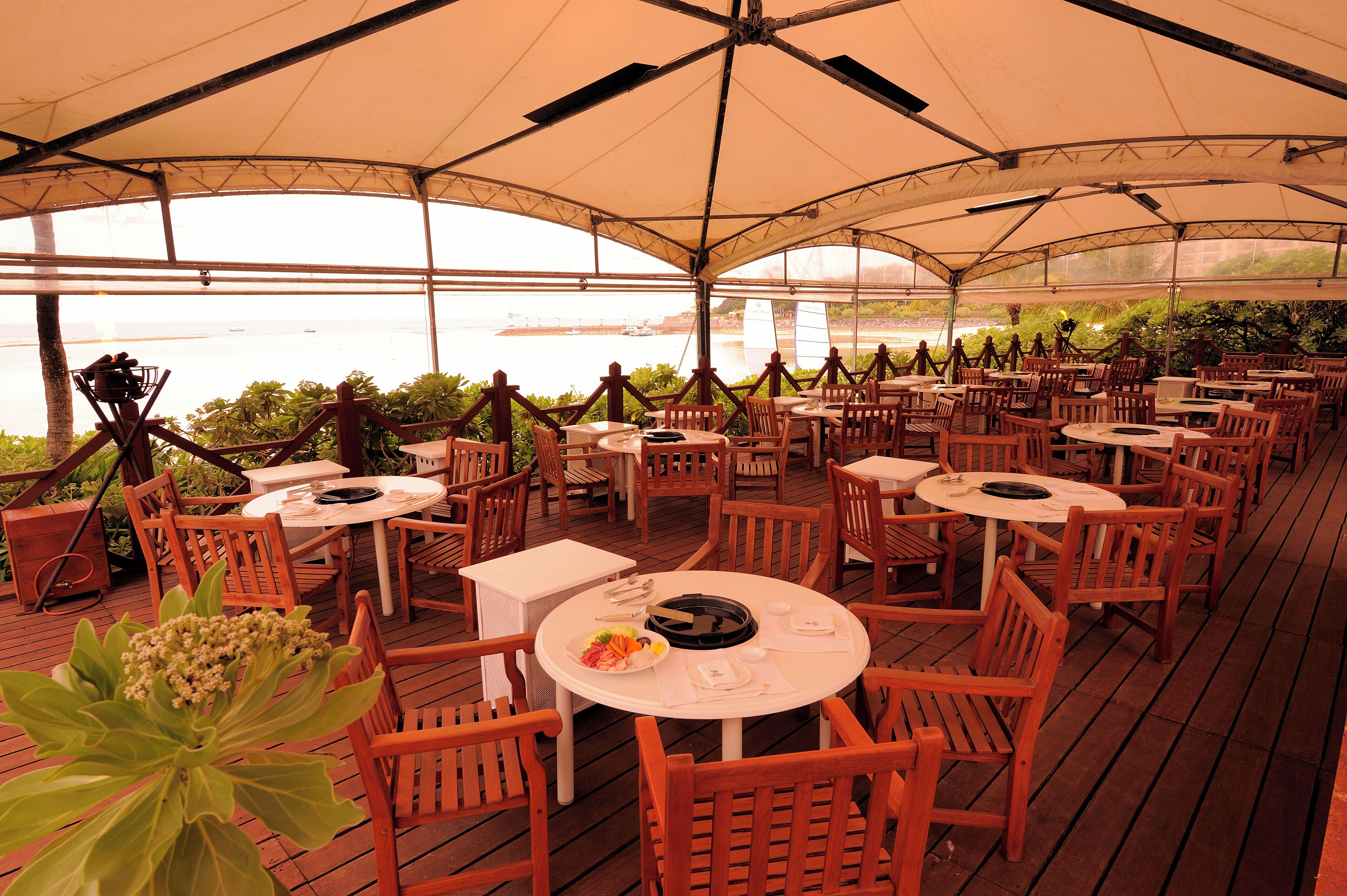 An outdoor dining area with tables and chairs, overlooking a body of water.