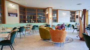 A spacious dining area with high ceilings, large windows, and a variety of seating options including green and orange chairs.