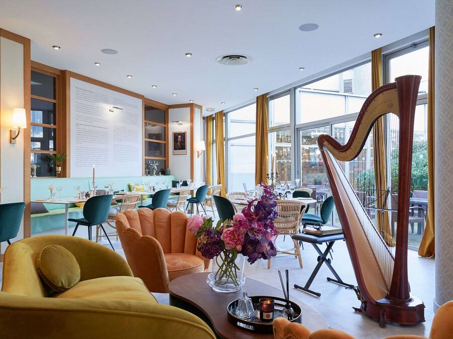 Un amplio vestíbulo de hotel con mobiliario moderno, un arpa y grandes ventanales con vistas al exterior.