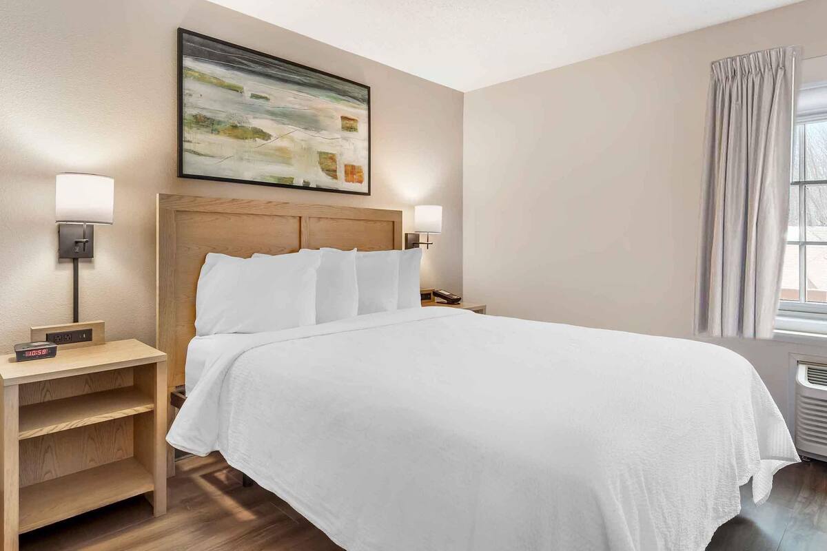 A neatly made bed with white linens, a wooden headboard, and two bedside lamps.